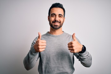 Young handsome man with beard wearing casual sweater standing over white background success sign...