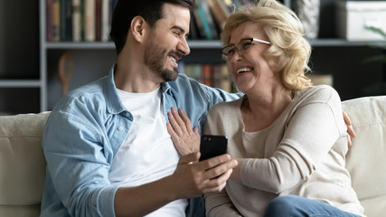 Overjoyed elderly mother and adult son relax using cellphone together