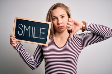Young blonde woman holding blackboard with smile message over isolated white background with angry...