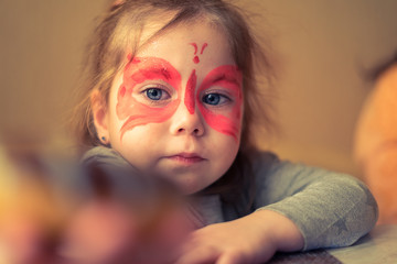 Little girl with a painted mask on her face in the form of pink butterflies