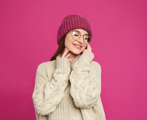 Young woman wearing warm sweater and hat on crimson background. Winter season