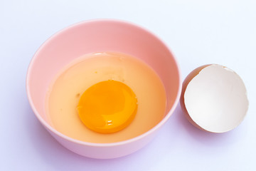 Egg yolk in a pink bowl with an eggshell on the white background