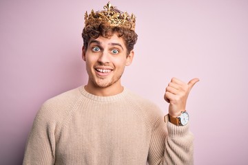 Young blond man with curly hair wearing golden crown of king over pink background smiling with...