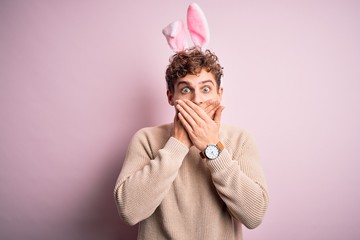 Young handsome blond man wearing easter rabbit ears over isolated pink background shocked covering mouth with hands for mistake. Secret concept.