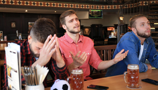 Sad male football fans watching game at bar and drinking beer.