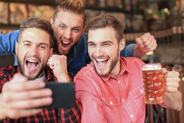 Diverse football fans watching football on smartphone and celebrating victory score in pub.