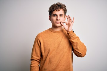 Young blond handsome man with curly hair wearing casual sweater over white background mouth and...