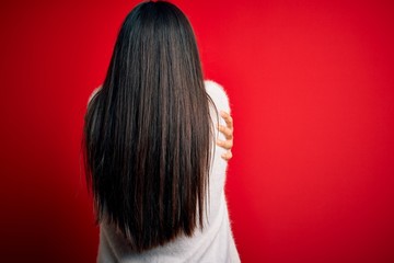 Young beautiful asian woman wearing casual sweater and glasses over red background Hugging oneself happy and positive from backwards. Self love and self care