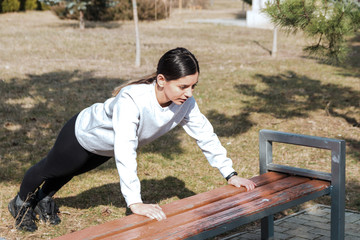 healthy lifestyle. cheerful attractive woman doing pushups on bench in park in the morning