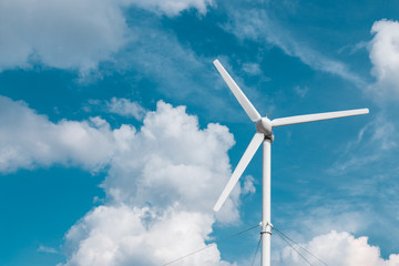 view of one wind turbine generator on blue sky with clouds and copyspace for text