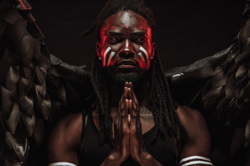 portrait of black angel praying with closed eyes isolated over black background. black angel pray for all mortals, for their good existence without sins