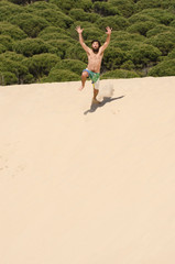 young man in swimsuit jumped on a sand dune on the beach in summer