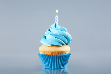 Delicious birthday cupcake with burning candle on light grey background
