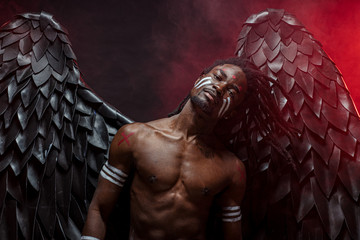 dark african angel with big black wings isolated, young serious muscular man wearing big wings on the back. strong angel come down from heaven. fantasy