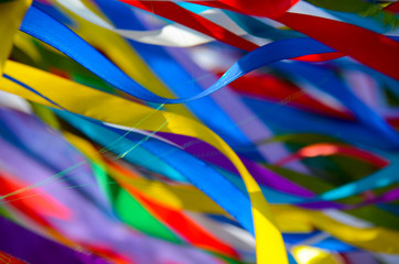Many multicolored ribbons flutter in the wind in the sun. background