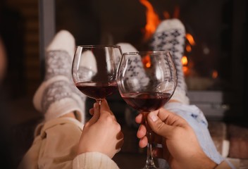 Couple with glasses of red wine near burning fireplace, closeup
