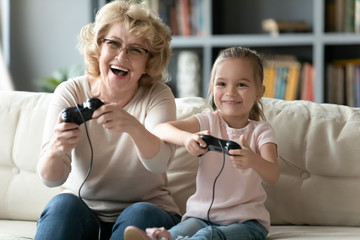 Modern grandmother play computer game with small granddaughter