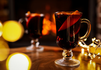 Tasty mulled wine, festive lights and blurred fireplace on background