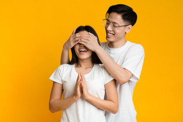 Naklejka premium Asian man standing behind his girlfriend and closing her eyes