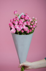 Beautiful bouquet of small roses in gray packing in a female hand on pink background. Closeup view