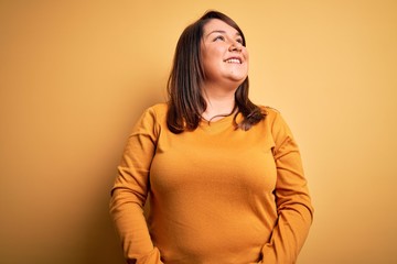 Beautiful brunette plus size woman wearing casual sweater over isolated yellow background looking...