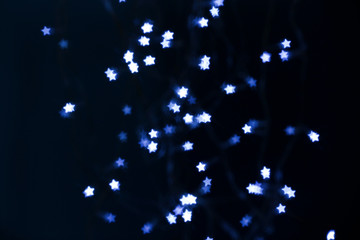 Blurred view of star shaped lights on black background. Bokeh effect