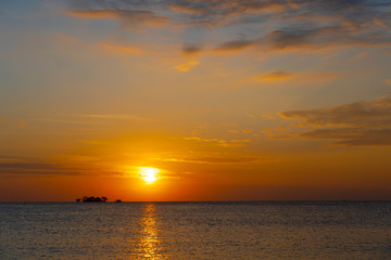 Fototapeta premium orange tropical sunset with little island on horizon line