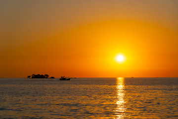 Fototapeta na wymiar orange tropical sunset with little island and fisherman boat on horizon line
