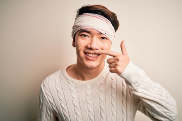 Young handsome chinese man injured for accident wearing bandage and strips on head Pointing with...