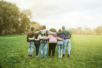Group of teenagers of different cultures hugging each other at the park at sunset - Teamwork of young people arranged from behind - Six men and women having fun together - 327343979