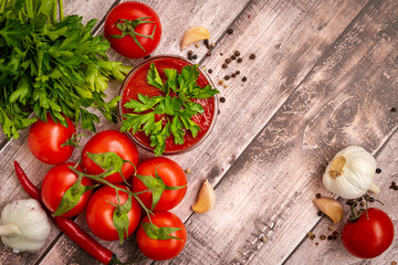 Bright, juicy, ripe tomatoes on a branch lie around ketchup in a sauce bowl on a wooden table with herbs, garlic, hot and allspice.