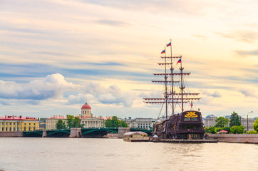 Obraz premium Cityscape of Saint Petersburg Leningrad with bascule Exchange Bridge, sailboat wooden ship with mast moored anchored on water of Neva river, evening dramatic orange sky background, Russia