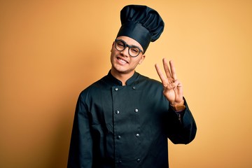 Young brazilian chef man wearing cooker uniform and hat over isolated yellow background showing and...