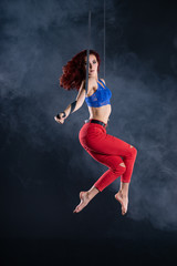 Fototapeta na wymiar Female athletic, sexy and flexible aerial circus artist with redhead on aerial straps on black background