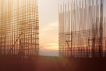 The construction of a rooftop high rise building, workers are tied with steel bars for concrete pouring, surveying the site and cranes are lifting or moving metal at the construction site. Pastel tone