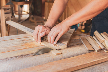 Close up, carpenter man cutting a plank of wood in the working using a circular saw in workshop.
