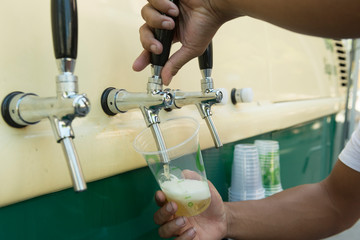 Bartender pouring from tap fresh beer into the plastic cup.
