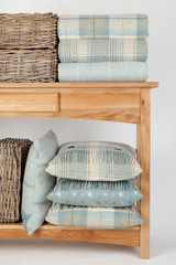 Sideboard style wooden beach table with blue coloured cushions, throws and wicker baskets on  white