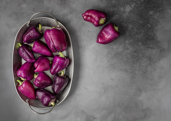 Fresh vegetables with water drops on a dark background. Sweet purple pepper in an oval metal plate...