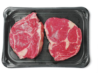 Two fresh premium rib eye steak in a vacuum pack package on a white background.