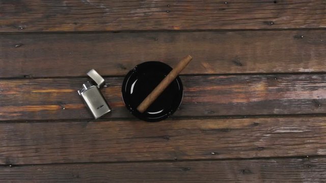 Camera crane shot. Approximation, cigar and lighter. Cigar on ashtray and silver lighter on a wooden table. Copy space.