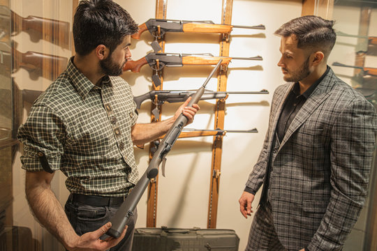 young customer and confident affable salesman discuss rifle power in guns store. people keen on firearm and hunting. armament