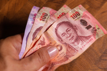 Male hand show 100 thai baht banknote, the official currency of Thailand. On front the portrait of the Rama or King,  Close up Paper Money of Thailand. 10th most frequently used world payment currency