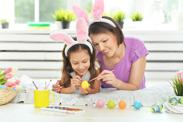 Obraz na płótnie Canvas Mother with daughter wearing rabbit ears decorating Easter eggs at home