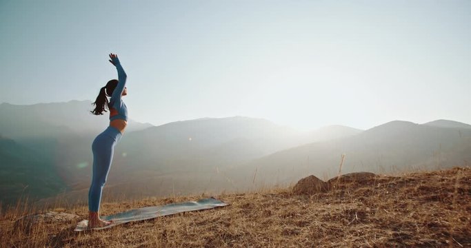 Yoga meditation in mountains. Fit girl doing yoga poses, having training session on cliff during sunrise - healthy way of life concept 4k footage