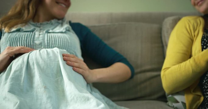 Two pregnant women sitting on sofa comparing their baby bumps
