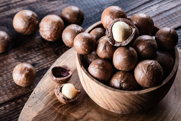 Organic ripe whole Macadamia nuts in bowl on old wooden rustic table.