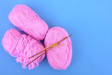  Pink woolen clews of thread and wooden knitting needles on a sky blue background
