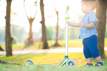 Little boy playing child scooter in city prak on green meadow © themorningglory