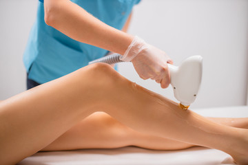 close-up photo of young woman getting laser hair removal procedure on her legs in modern clinic. cosmetology and spa, skin care concept